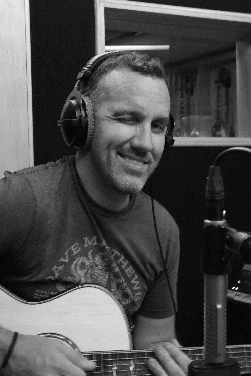 Craig smiling with his guitar and headphones in the recording studio