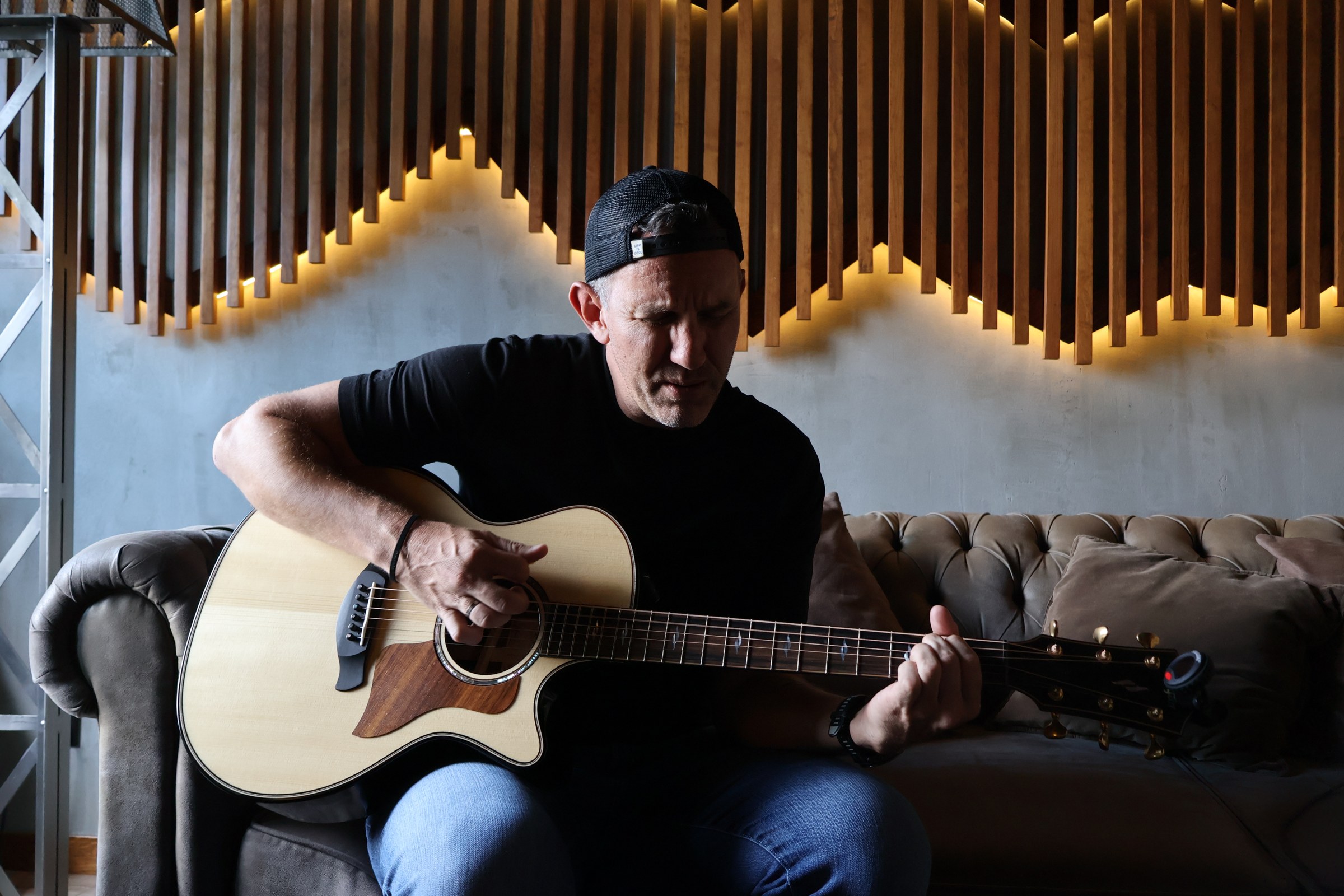 Craig Connors playing an acoustic guitar on a studio sofa